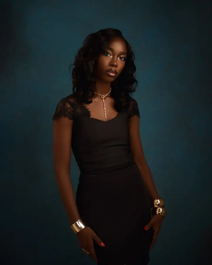 A woman in a black lace dress stands against a deep teal studio backdrop, shot by Emerald Shot It