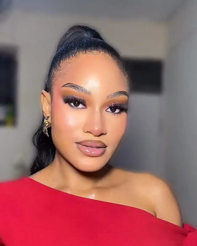 A woman in a red off-shoulder dress with a high ponytail, smoky eyes and a pink lip