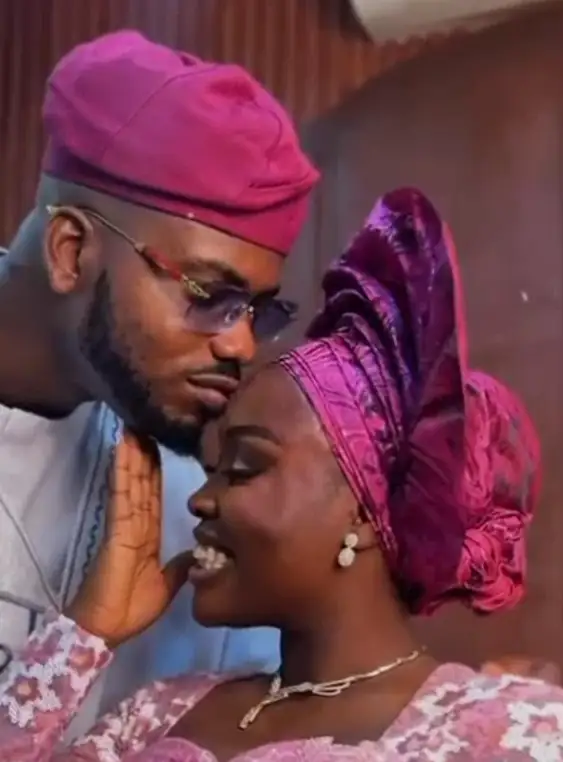 A bride in a fuchsia gele leans into her groom in a matching cap, both glammed for the day